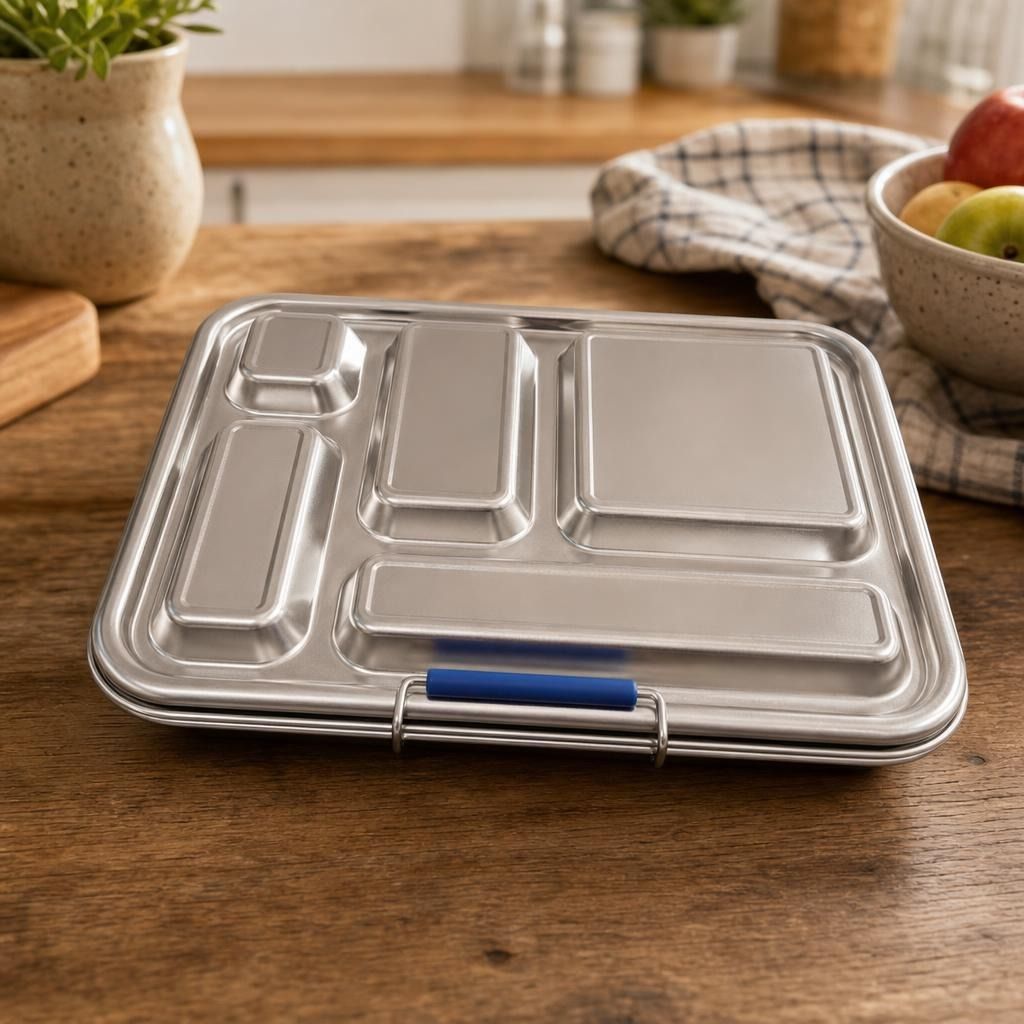 Close-up of a large stainless-steel lunchbox with five compartments on a wooden table, highlighting its sleek, polished surface and clean lines.