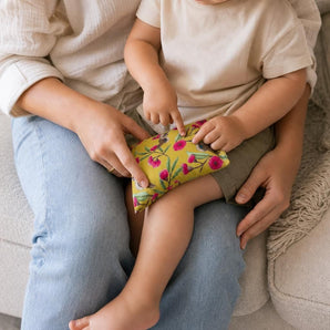 Toddler sitting on adult's lap using Small Comfy Critters Lupin Pack Kookaburra for knee support in cozy lounge.