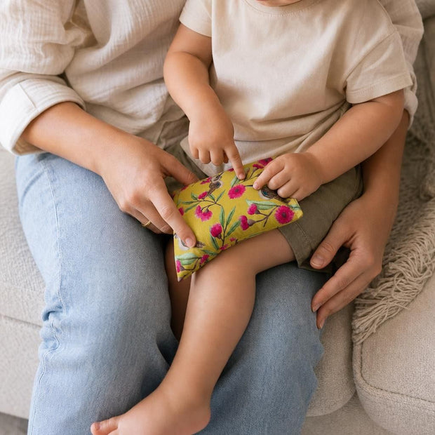 Toddler sitting on adult's lap using Small Comfy Critters Lupin Pack Kookaburra for knee support in cozy lounge.